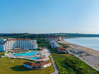 Grande resort alberghiero su una lunga spiaggia sabbiosa con più piscine e prati verdi.