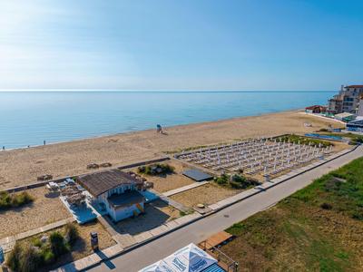 Spiaggia con sabbia, lettini, padiglioni e edifici vicino all'acqua sotto un cielo azzurro.