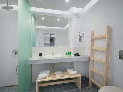 Bagno moderno con grande specchio, mensola in legno e asciugamani bianchi in un hotel.