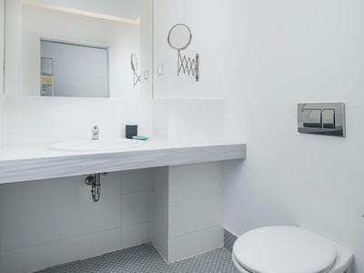 Bagno moderno e luminoso con WC sospeso, grande specchio e pareti bianche.