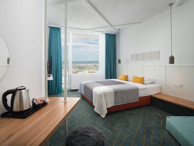 Camera d'hotel moderna con letto matrimoniale, ampia finestra e vista sulla città.