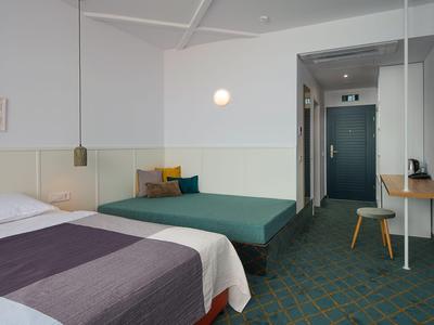 Una camera d'hotel semplicemente arredata con letto matrimoniale, zona salotto e tappeto verde-blu.