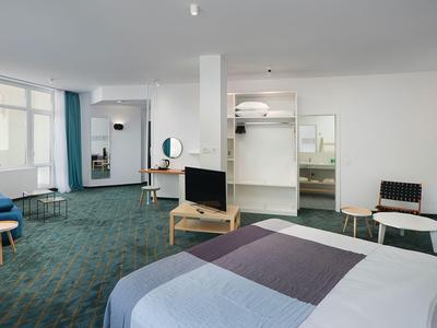 Camera d'hotel moderna con letto grande, zona salotto e area lavoro alla luce del giorno.