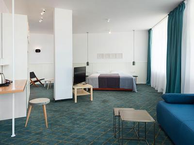 Ampia camera d'hotel luminosa con moquette blu, divano, letto e due piccoli tavoli.