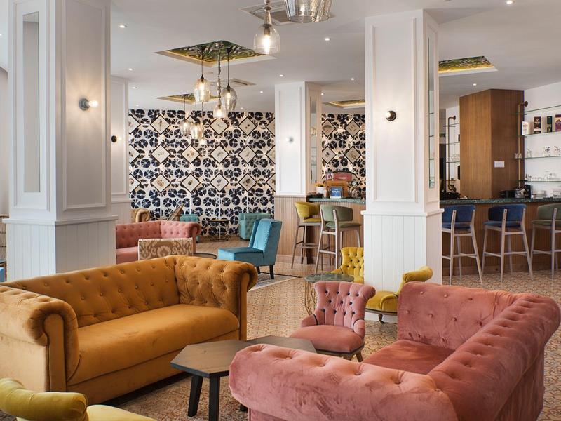 Helles Wohnzimmer mit bunten Samtsofas, gemusterten Teppichen und stilvollen Pendelleuchten.