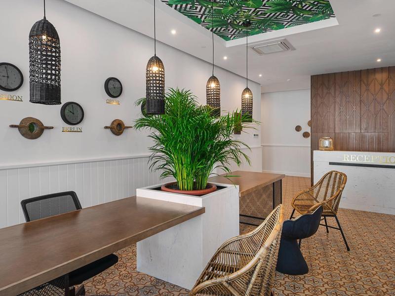 Moderner Essbereich mit Holz- und Rattanstühlen, Pflanzen und schwarzen Hängeleuchten an weißer Wand.