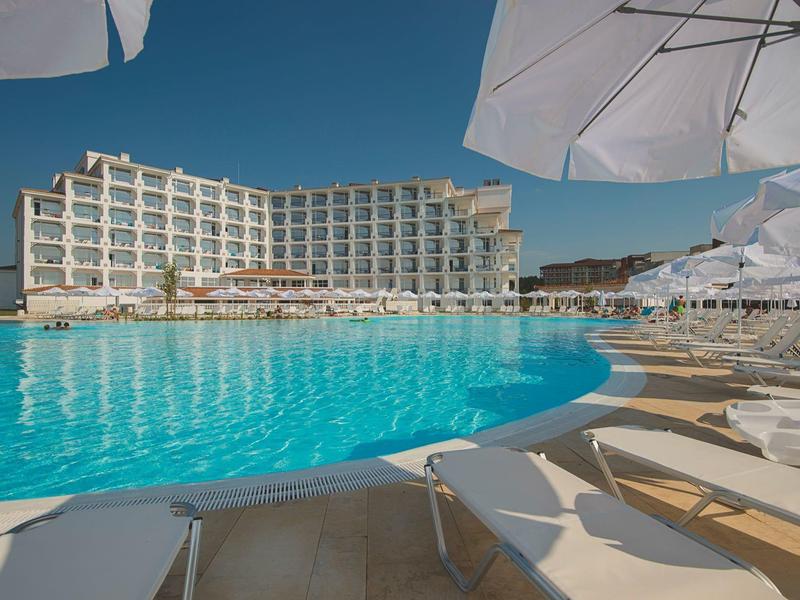 Moderner Hotelkomplex mit großem Außenpool und weißen Sonnenschirmen.