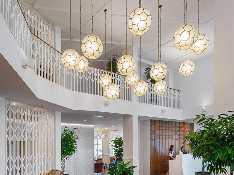 Moderner heller Raum mit hängenden Kugelleuchten, braunen Sesseln und grünen Pflanzen, offene Galerie.