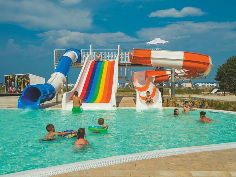 Mehrere Menschen schwimmen in einem Pool mit bunten Wasserrutschen an einem sonnigen Tag.