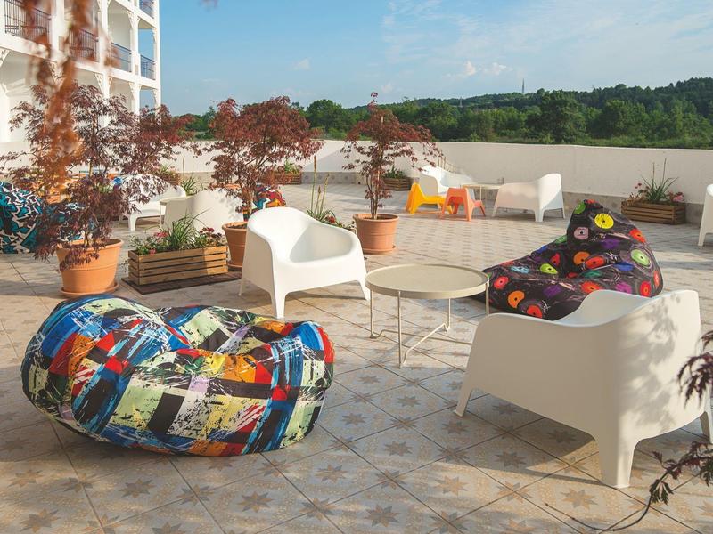 Terrasse mit buntem Sitzsack, weißen Stühlen und Pflanzen mit Blick auf grüne Hügel.