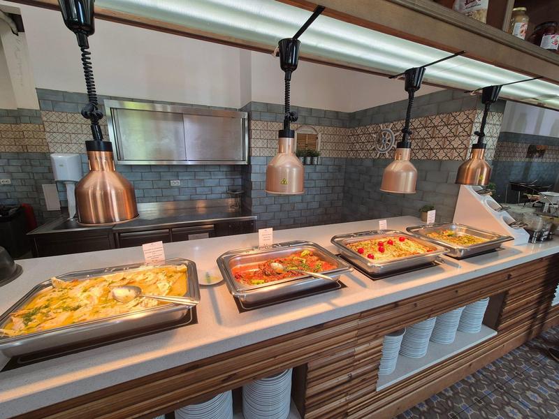 Buffet mit warmen Speisen, darunter Auflauf, Gemüse und Eintopf, in einem modernen Gastraum.