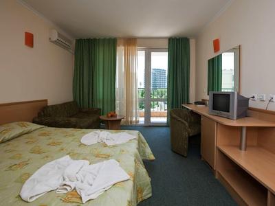 Hotel room with double bed, green curtains, balcony, and basic TV.
