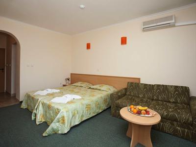 Hotel room with two single beds, sofa, small table, and wall-mounted air conditioner.