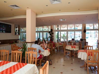 Bright dining room with wooden tables and chairs, guests eating, and large windows.
