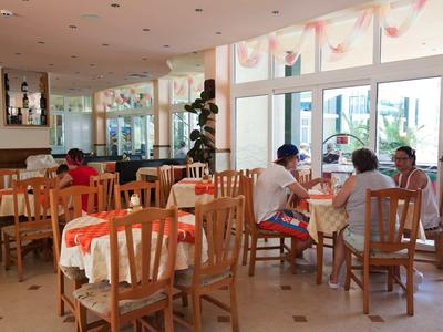 Bright restaurant with wooden furniture and large windows, guests seated at tables.