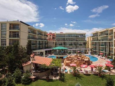 Hotel con varios edificios alrededor de una piscina con sombrillas y jardín.