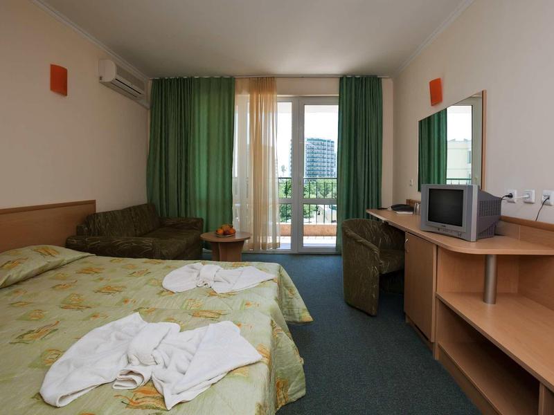 Hotel room with double bed, green curtains, balcony, and basic TV.