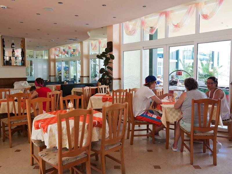 Bright restaurant with wooden furniture and large windows, guests seated at tables.