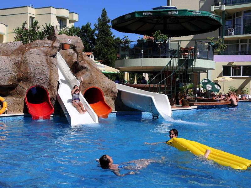 An outdoor pool with multiple water slides and swimmers, surrounded by hotel buildings.
