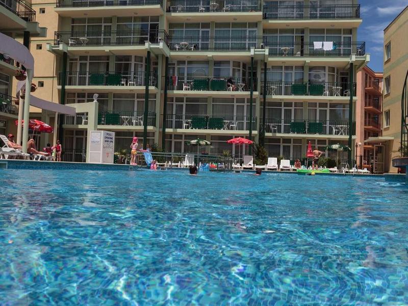 Modern hotel complex with large outdoor pool under blue sky.