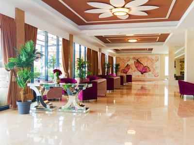 Heller Hotel-Lobby mit Marmorfußboden, großen Fenstern, Pflanzen und violetten Sesseln.