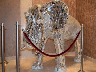 Große Elefantenfigur aus glitzernden Spiegelstücken, umgeben von rotem Absperrband und Metallpfosten.