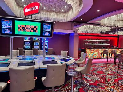 Modernes Casinointerieur mit Roulettetisch, Stühlen und einem farbenfrohen Teppich.