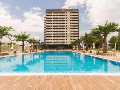 Ein moderner Hotelkomplex mit großem, klarem Pool und Palmen auf beiden Seiten.