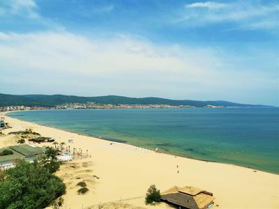 Weiter Sandstrand mit klarem Wasser und bewaldeten Hügeln im Hintergrund unter blauem Himmel
