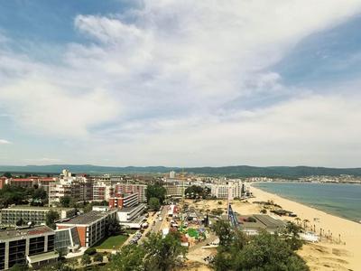 Stadtansicht mit Strand, Sand, Gebäuden, Bergen und bewölktem Himmel im Hintergrund.