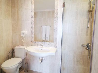 Kleines Badezimmer mit weißer Toilette, Waschbecken, großem Spiegel und Glas-Duschkabine.