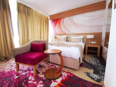 Gemütliches Schlafzimmer mit Doppelbett, rosa Sessel, runden Tischen und buntem Teppich.