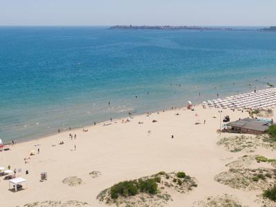 Breiter Sandstrand mit Menschen, Liegestühlen und blauem Meer unter klarem Himmel.