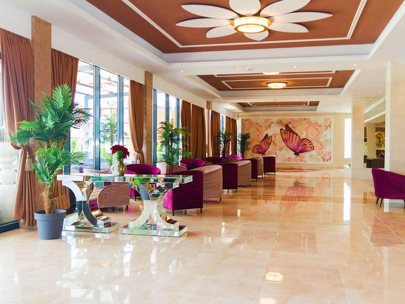 Heller Hotel-Lobby mit Marmorfußboden, großen Fenstern, Pflanzen und violetten Sesseln.