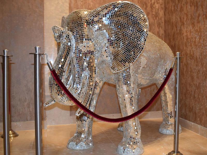 Große Elefantenfigur aus glitzernden Spiegelstücken, umgeben von rotem Absperrband und Metallpfosten.