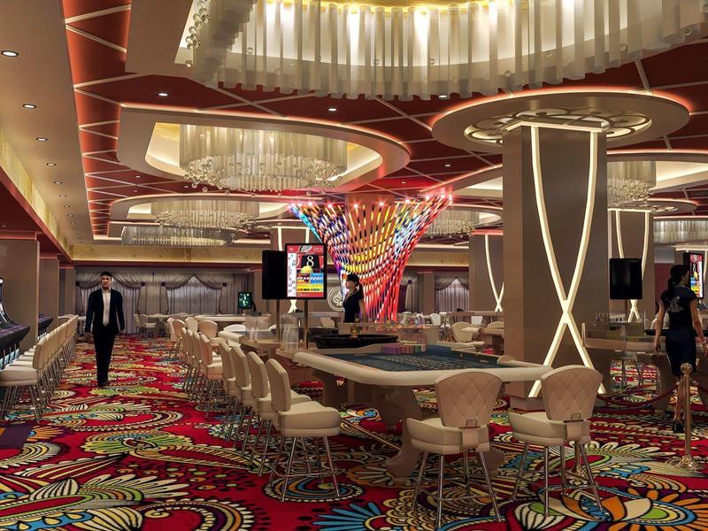 Großer, heller Casinosaal mit farbigem Teppich, Spieltischen, Stühlen und modernen Deckendesigns.