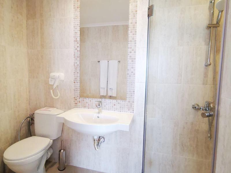 Kleines Badezimmer mit weißer Toilette, Waschbecken, großem Spiegel und Glas-Duschkabine.