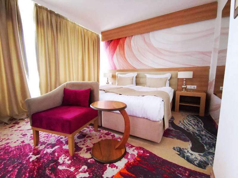 Gemütliches Schlafzimmer mit Doppelbett, rosa Sessel, runden Tischen und buntem Teppich.