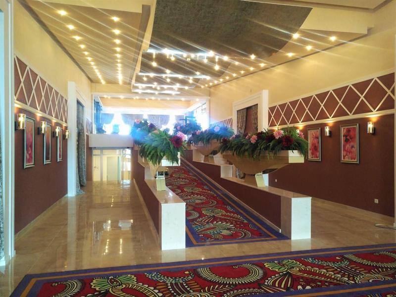 Langer Innenraum mit Teppich, dekorativen weißen Trennwänden, Pflanzen und leuchtenden Lichtern.