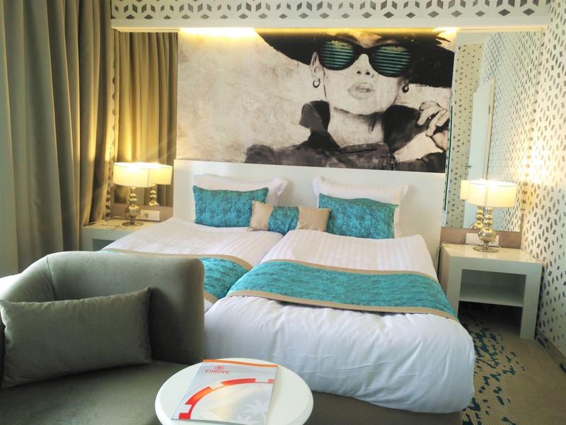 Modern eingerichtetes Schlafzimmer mit großem Bett, türkisfarbenen Kissen und gemütlichem Sessel.