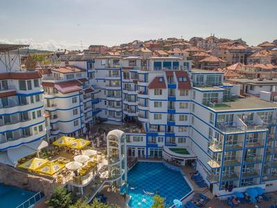Grande hotel con piscina, più edifici e lettini in una città costiera.