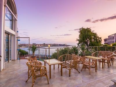 Terraza con sillas de mimbre y mesas con vista al río y la ciudad al atardecer.