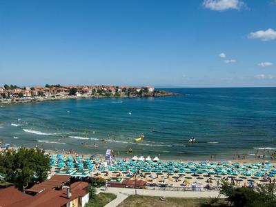 Playa soleada con muchas tumbonas con vistas al mar y una ciudad costera.