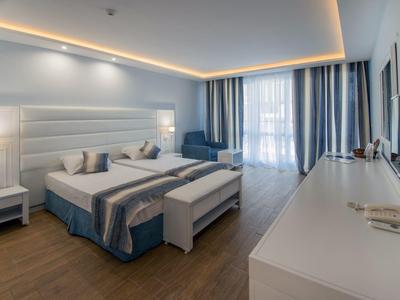 Camera d'hotel moderna con letto matrimoniale, zona salotto e grande finestra con tende.