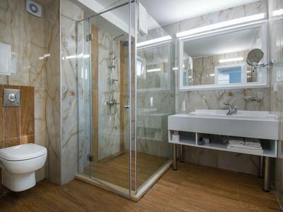 Bagno moderno con doccia in vetro, WC sospeso e grande specchio sopra il lavabo.