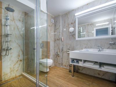 Bagno luminoso con doccia walk-in, WC e lavandino con specchio illuminato.