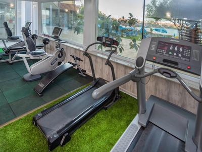 Gimnasio con cinta de correr y bicicletas, grandes ventanales con vista a la piscina y área exterior.