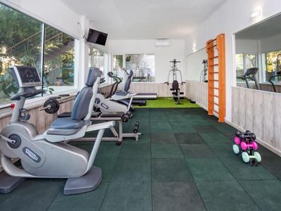Gimnasio moderno con equipo de ejercicio y pesas en una sala luminosa con grandes ventanas.