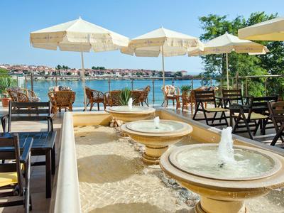 Terrazza con tavoli sotto ombrelloni e fontane, vista sulla città costiera sullo sfondo.