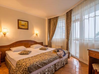 Camera d'hotel luminosa con letto matrimoniale, tende e scrivania accanto a grandi finestre.